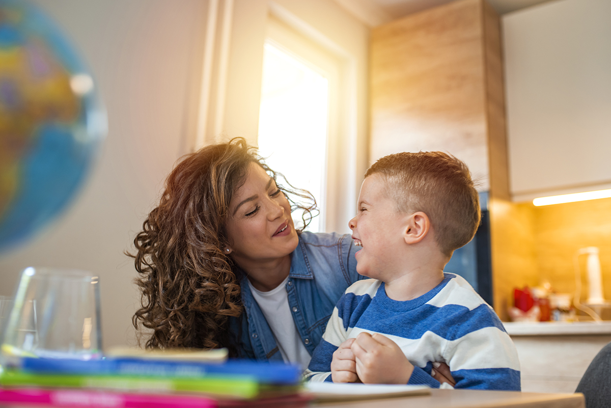 Kind mother helping her son doing homework in kitchen.