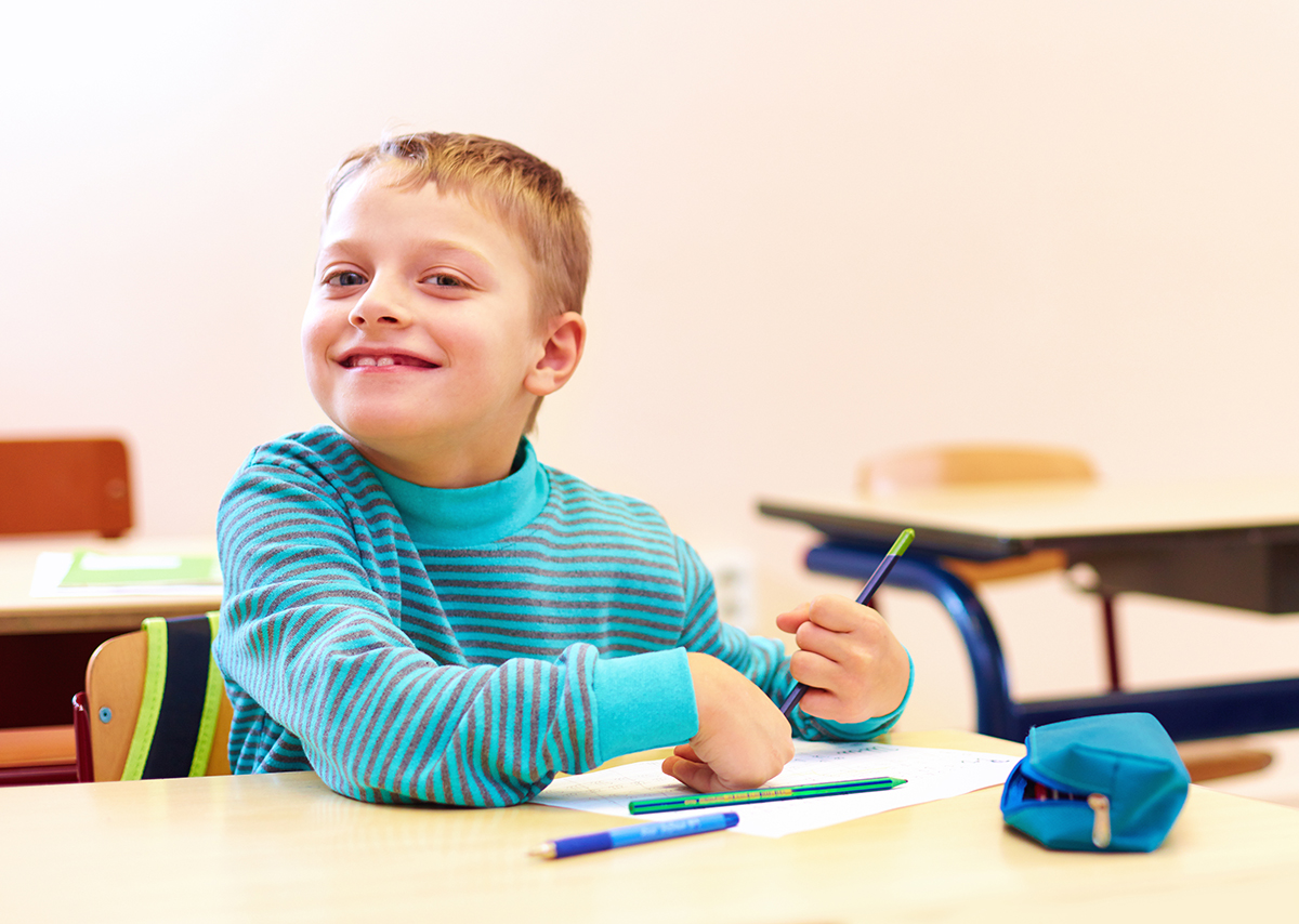 cute boy with special needs writing letters while sitting at the desk in class room